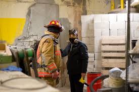 A firefighter standing inside a building. A man wearing a breathing mask stands next to him.