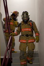 Two firefighters in protective suits walk down a staircase.
