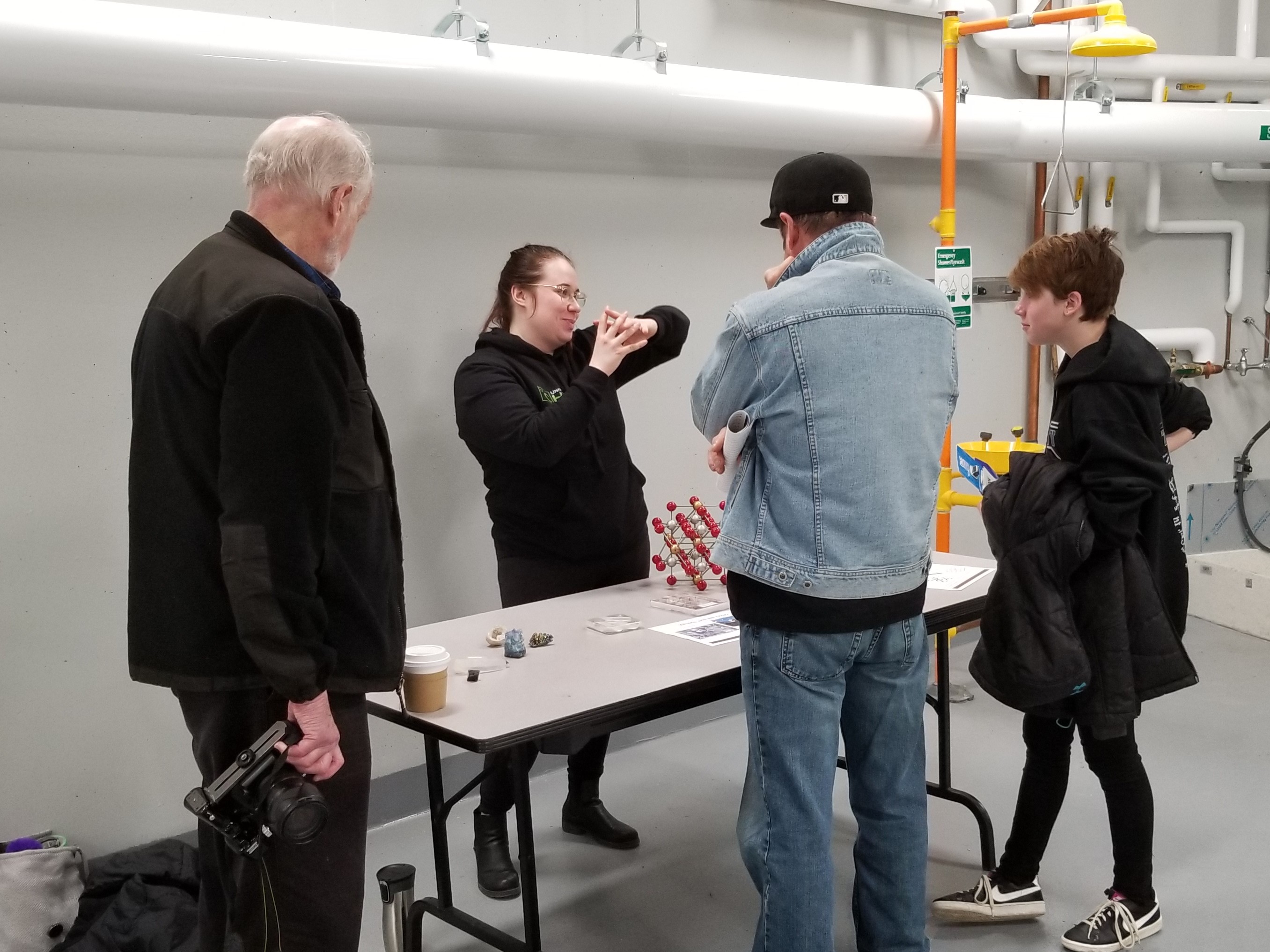 A researcher discusses an atom model with three visitors. 