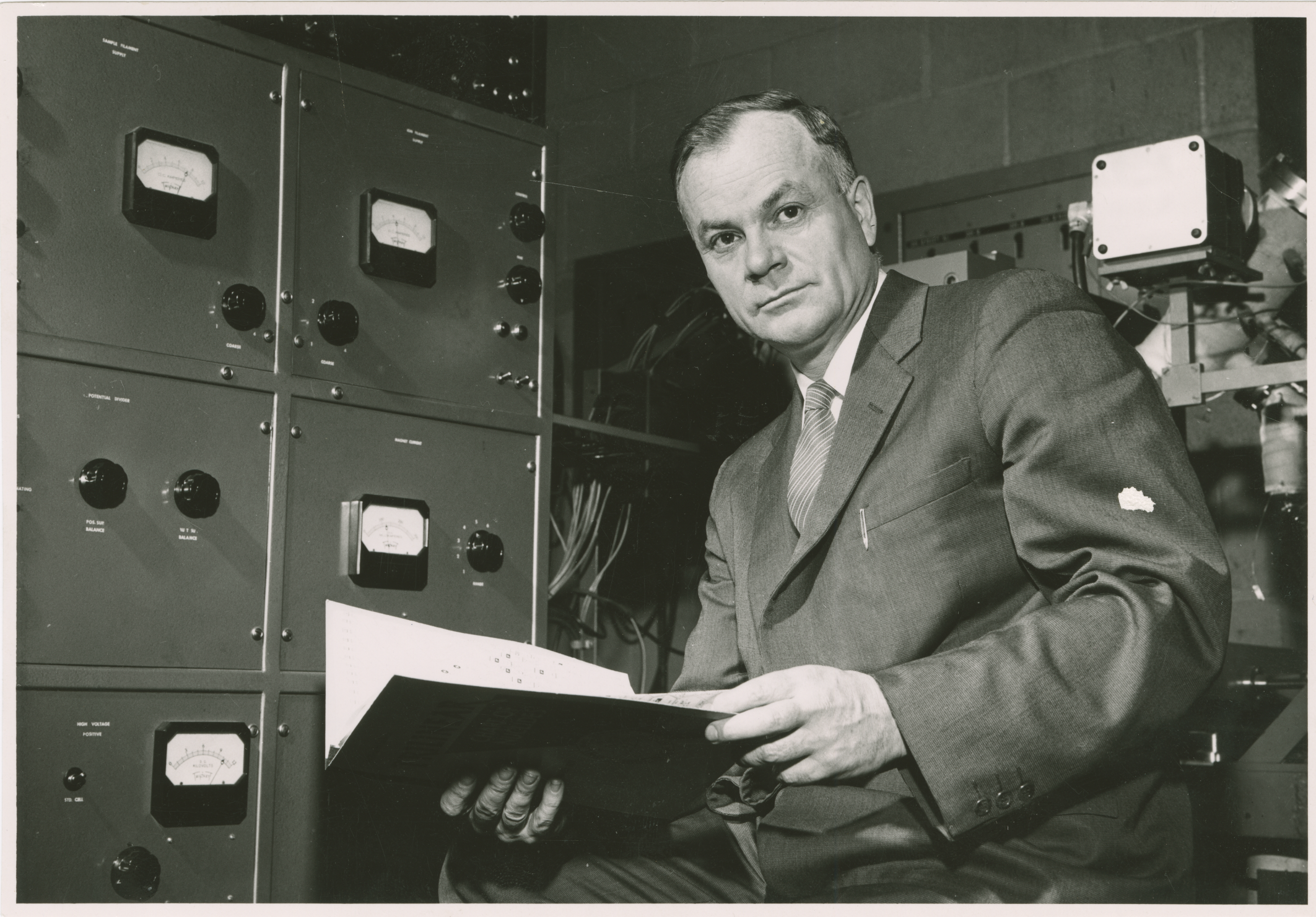 Harry Thode holding a book and sitting in the control room of McMaster Nuclear Reactor
