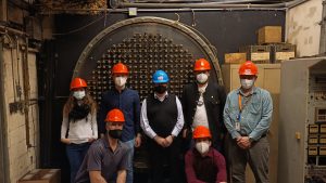 A group of people wearing hardhats stand in front of machinery.