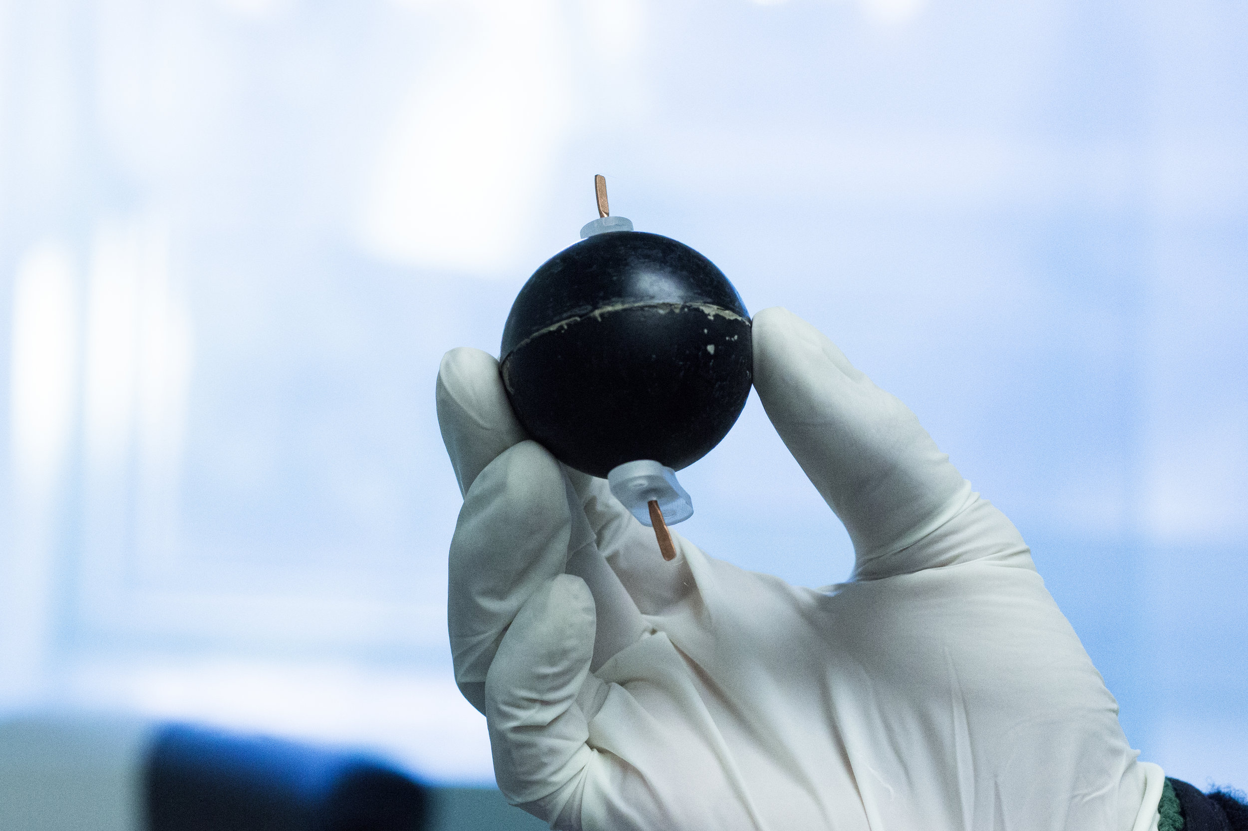 A gloved hand holds a TEPC, which looks like a small black sphere. 