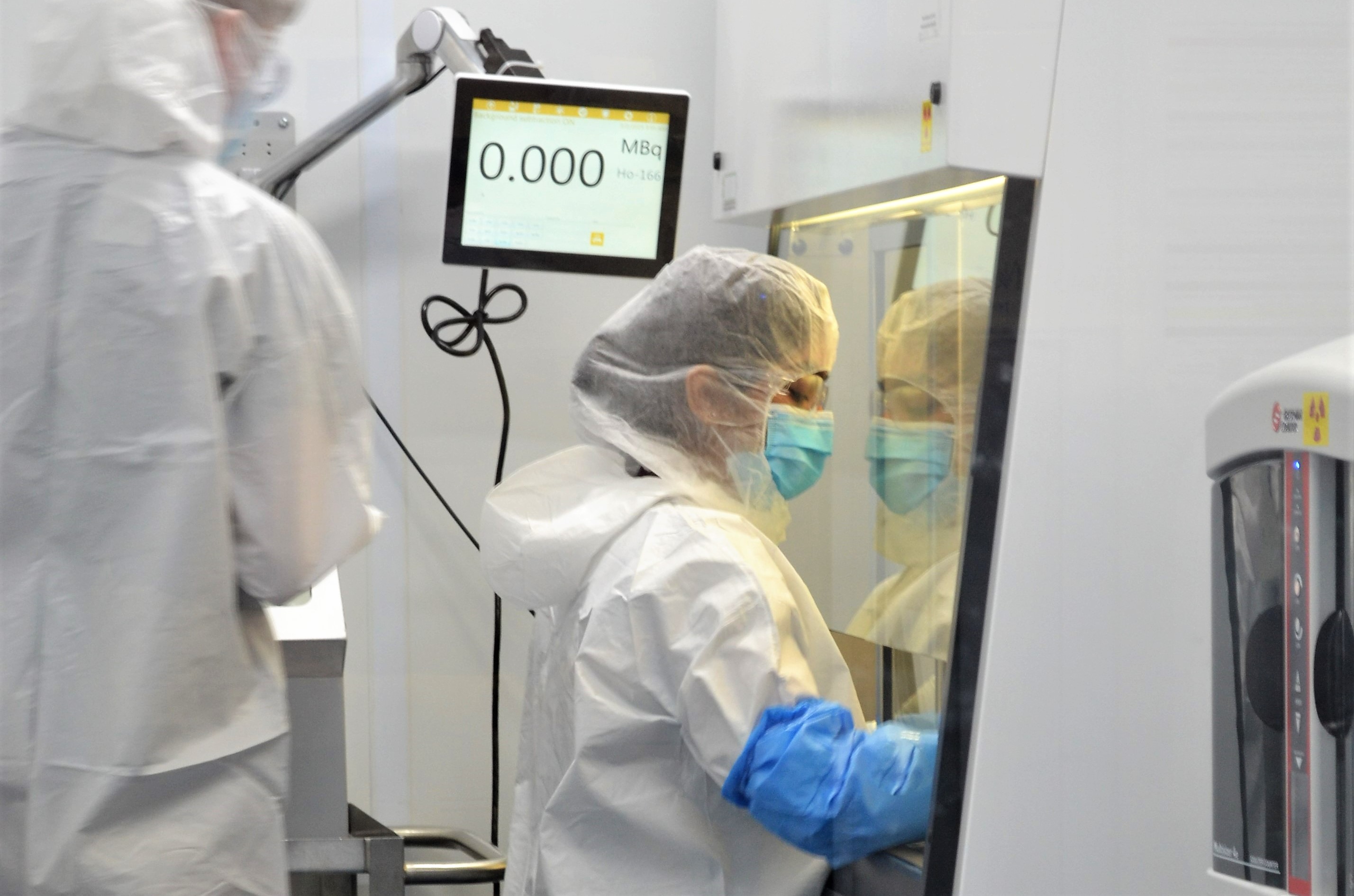A technician wearing PPE dispenses a medical isotope inside a lab.
