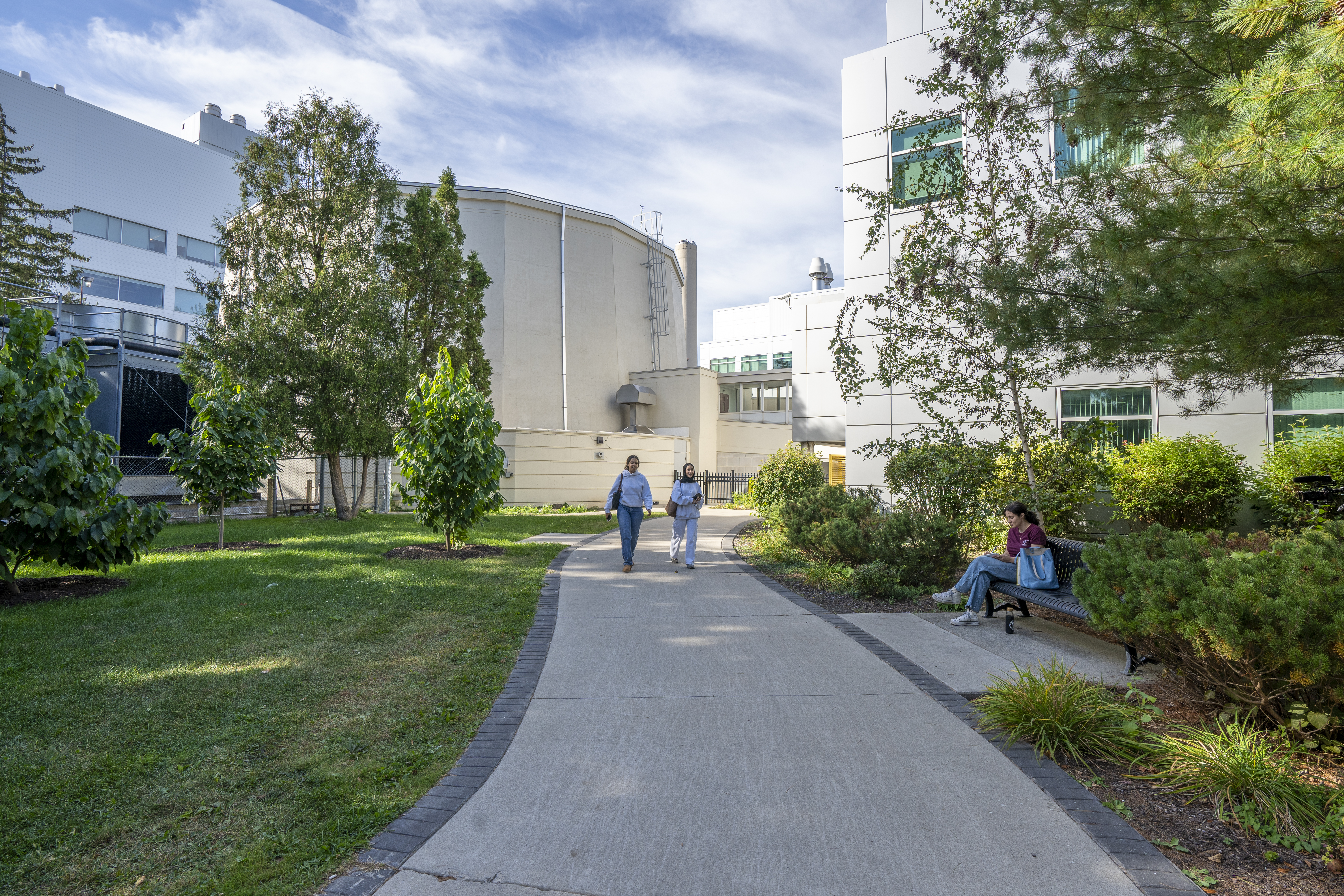 Two students walk on a paved pathway; the McMaster Nuclear Reactor containment building is behind them.